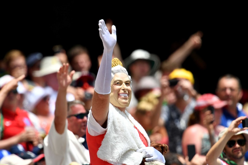 A person wearing a mask depicting Queen Elizabeth II is seen in the crowd