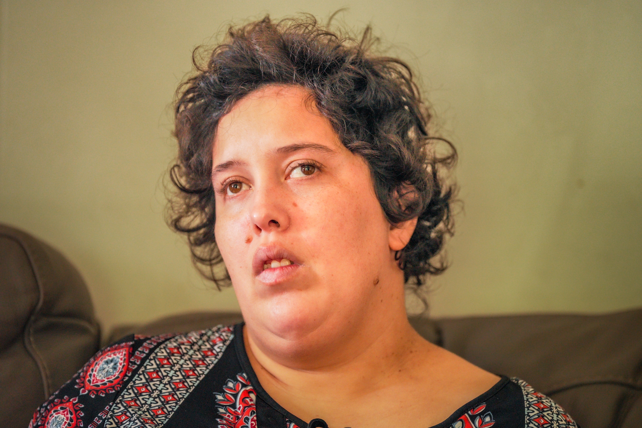 A woman with short brown hair wearing a black and red patterned blouse.