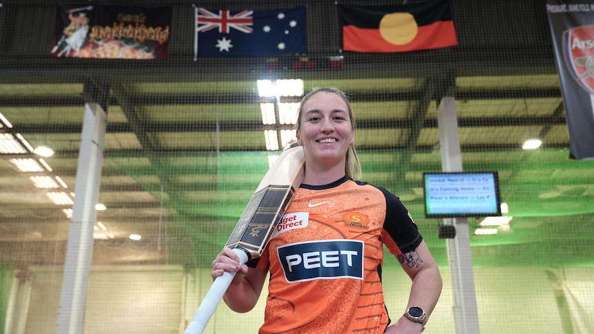 Mikayla Hinkley smiling wearing her orange Scorchers shirt with the Australian and Aboriginal flags in the background.