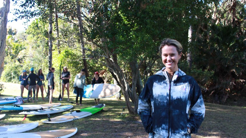 Kayaker Hayley Talbot standing in front of Stand-up paddle boards at Women's Adventure Summit.