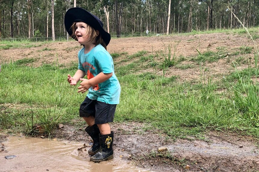 A young girl jumps in a muddy puddle.