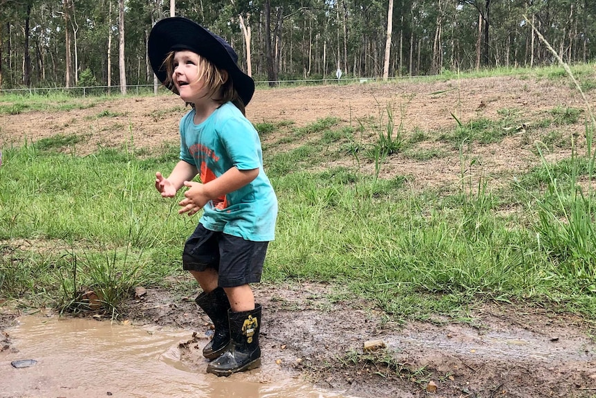 A young girl jumps in a muddy puddle.