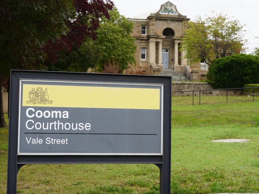 A sign that reads "Cooma Courthouse". Behind it is an imposing, historic-looking stone building.