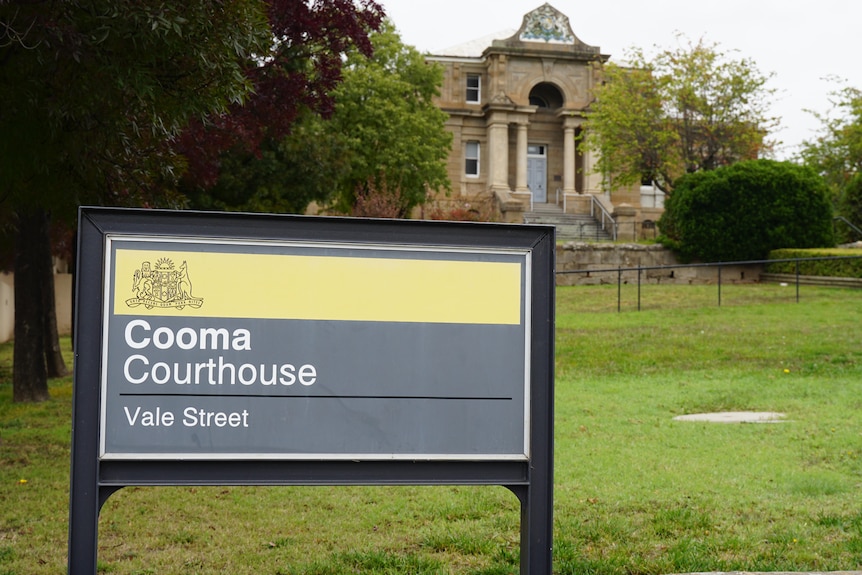 A sign that reads "Cooma Courthouse" in front of a historic-looking building. 