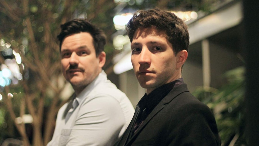 Two men sitting on a bench, looking at the camera.