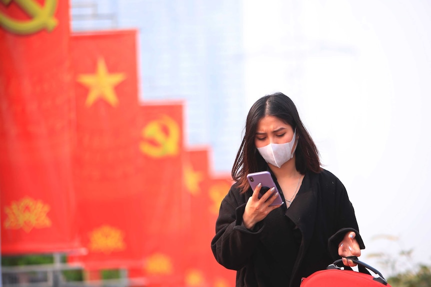 A woman glances down at her phone with Vietnamese flags in the background.