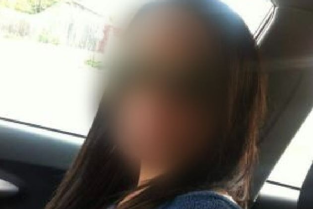 A woman with long dark hair, her face is blurred, sitting in a car.