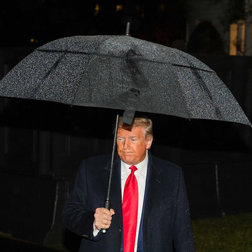 Donald Trump looking grim while carrying an umbrella