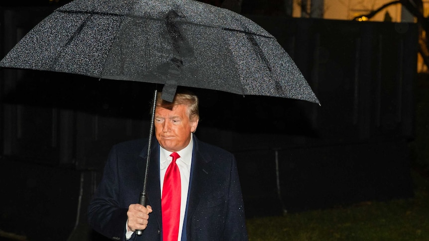 Donald Trump looking grim while carrying an umbrella