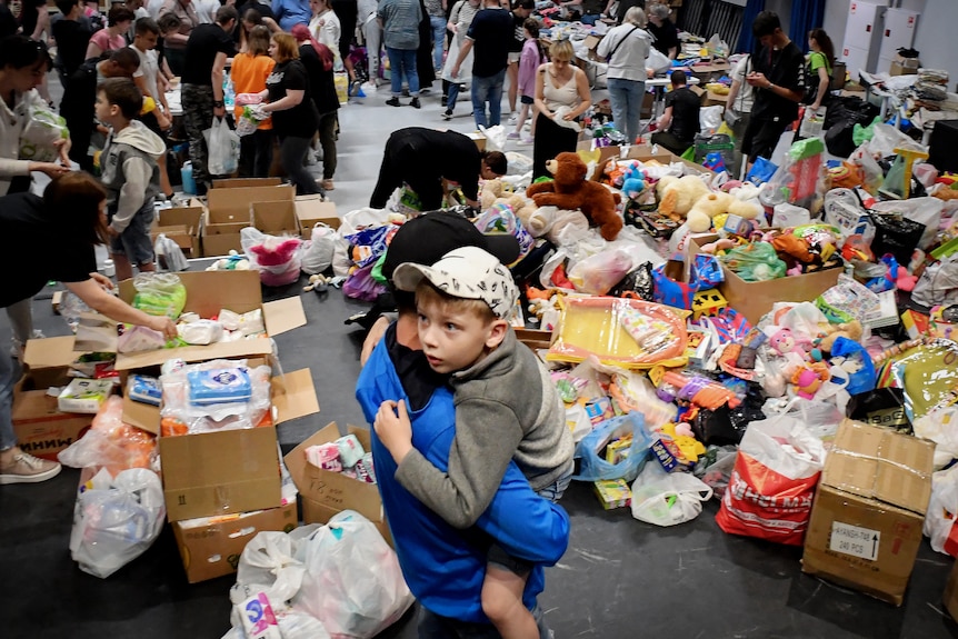 A child is held by an adult in a shelter where goods are being distributed to people who have evacuated