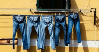 A row of denim jeans hang on the line against a yellow wall to depict theories about denim, such as buying jeans too tight.