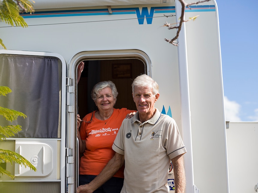 A couple lean out of the side door of their motor home, smiling.