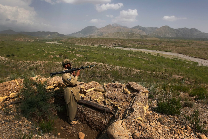 A Pakistani soldier holds a rocket launcher in front of beautiful rolling mountains near the Pakistan/Afghanistan border.