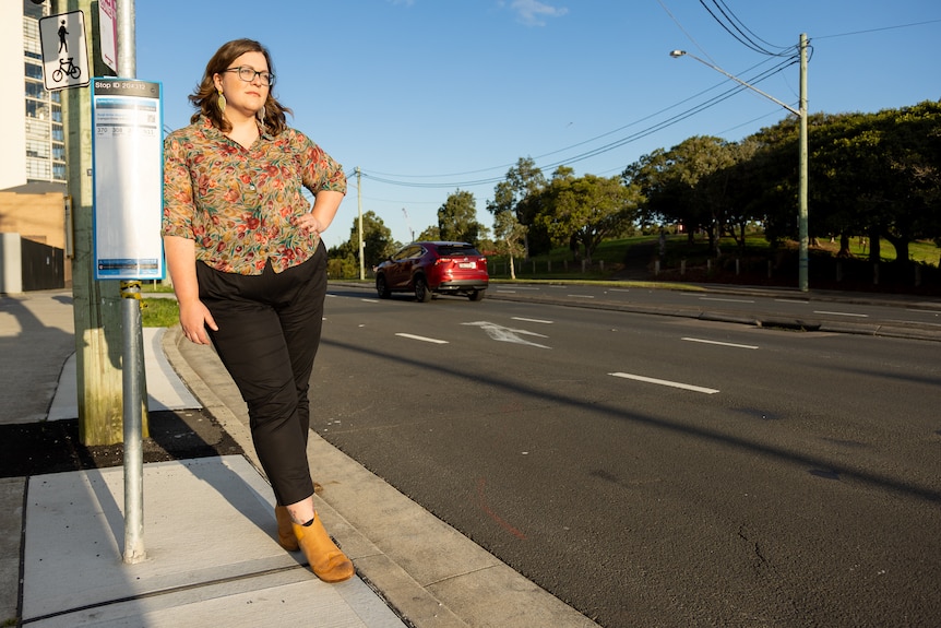 A woman stands at a bus stop next to a highway