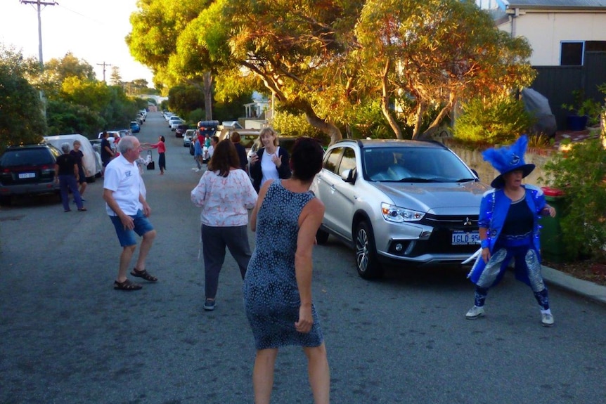 Adults dance on narrow street between parked cars
