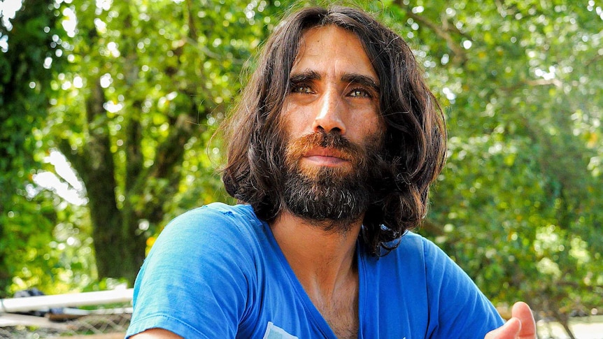 A picture of a long-haired man wearing a blue t-shirt.