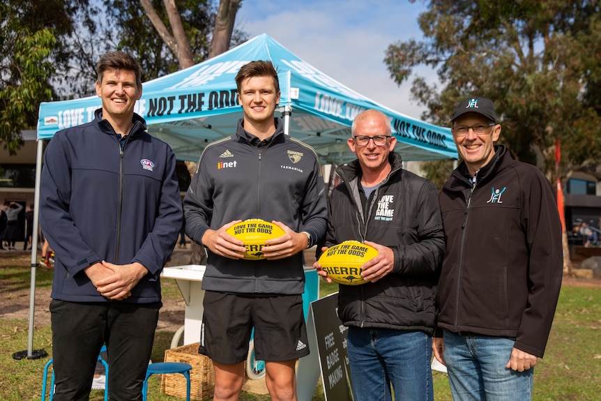 Four men smile at the camera, holding AFL balls.