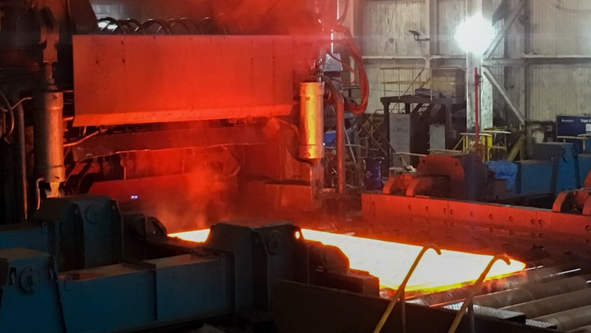 A hot steel plate exits the milling press