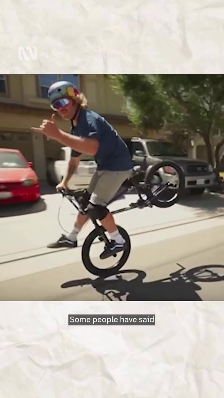 Young man rolls on front wheel of BMX while doing the shaka with one hand and steering with the other