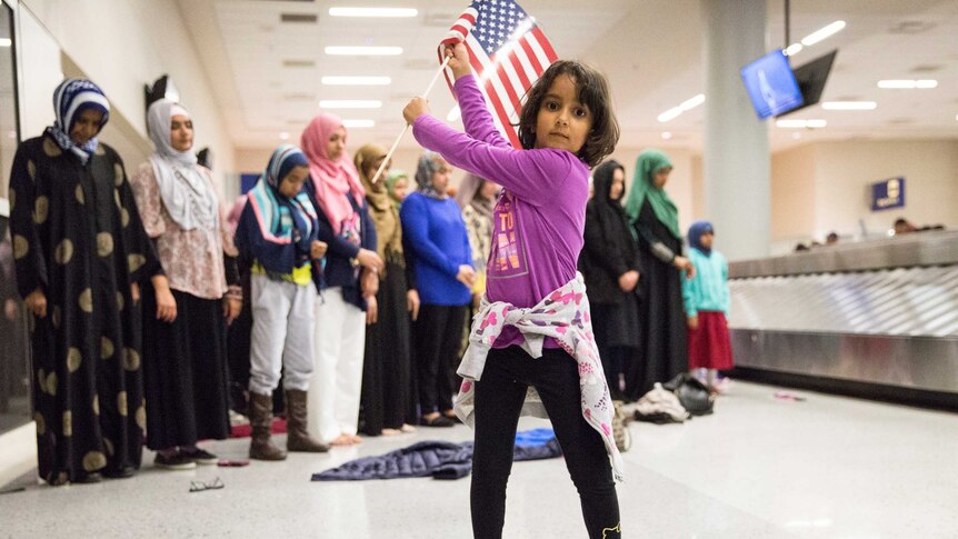 A young girl dances with an American flag in the baggage claim area of Dallas airport.
