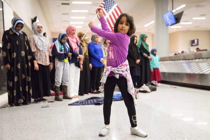 A young girl dances with an American flag in the baggage claim area of Dallas airport.