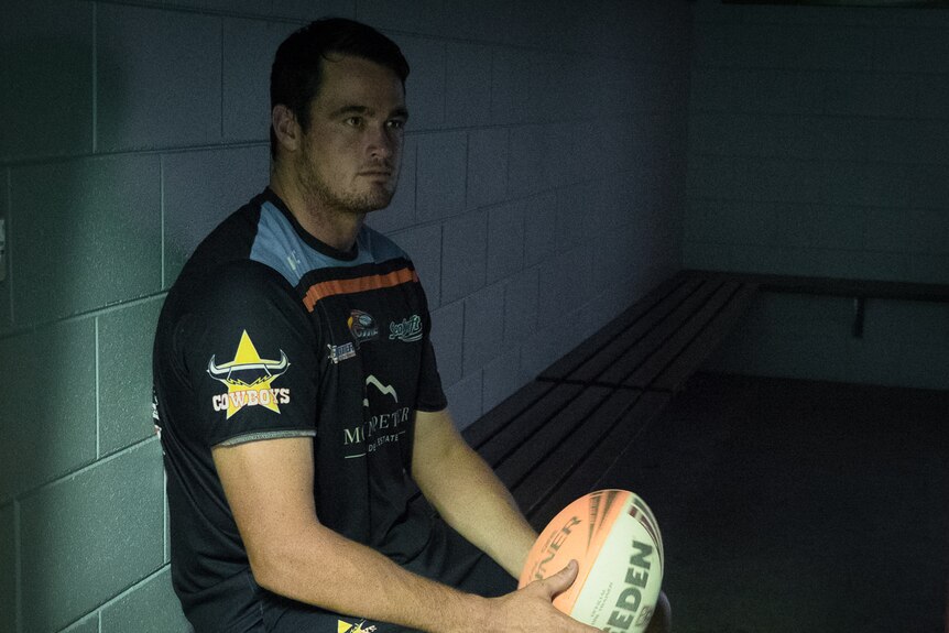 Man with football sitting alone in dark dressing room.