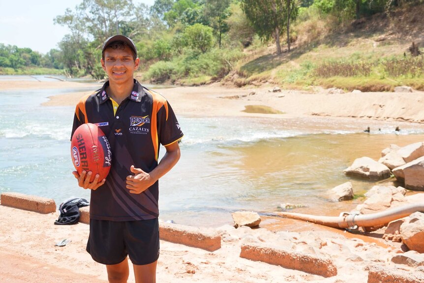 Adam Sambono holds a football beside the Daly River.
