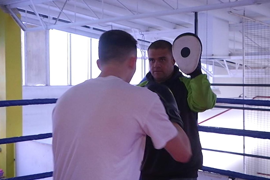 A boxing coach holding pads for a young man, who is wearing boxing gloves and is ready to punch