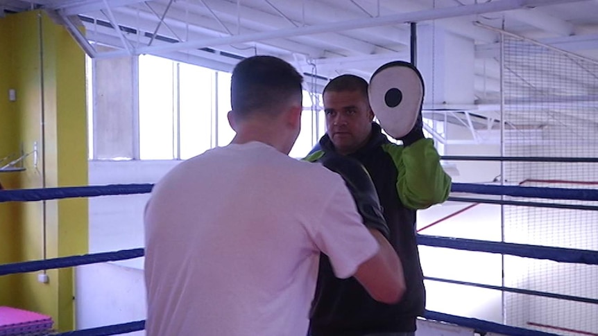 A boxing coach holding pads for a young man, who is wearing boxing gloves and ready to punch