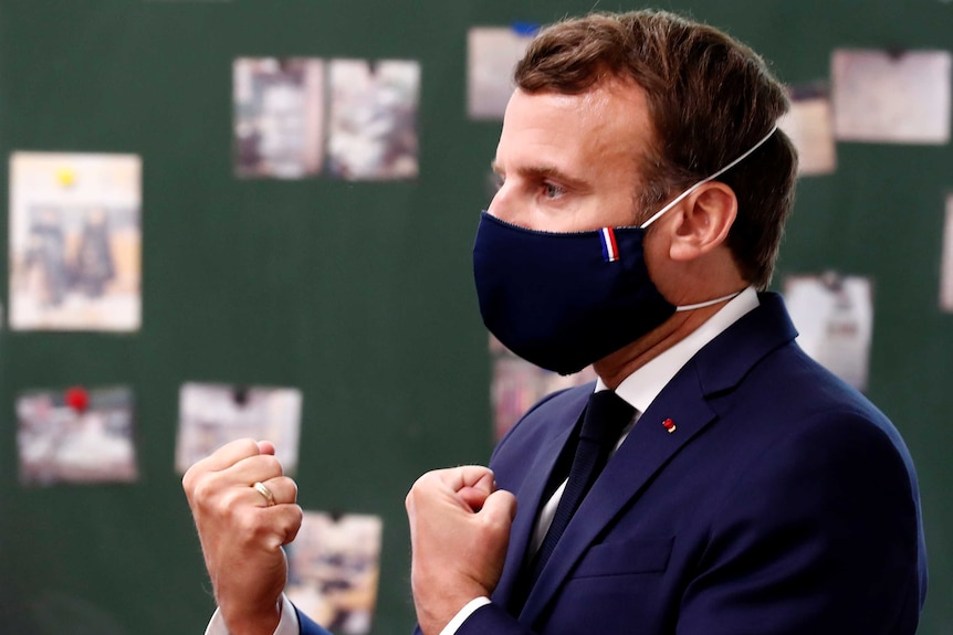 French President Emmanuel Macron clenches both fists as he wears a mask in a classroom.