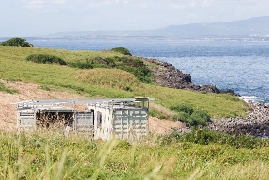 The island has two shipping containers which serve as storage areas for workers. It has a rocky shoreline.