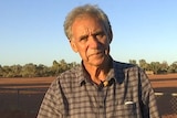 ABC Sports Broadcaster Charlie King stands in front of a dirt football oval in the Northern Territory.