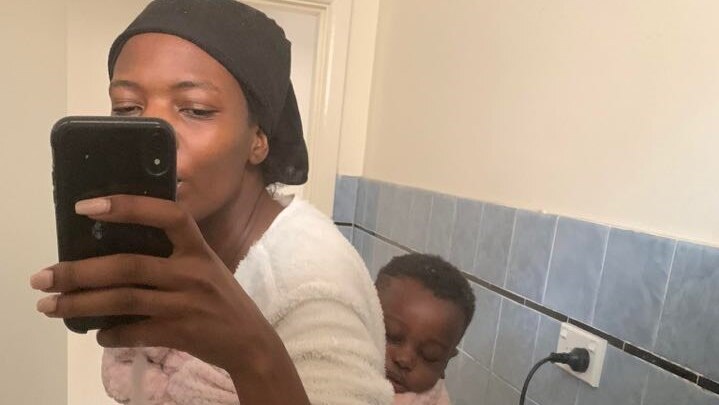 A woman takes a selfie while baby-wearing in her bathroom.