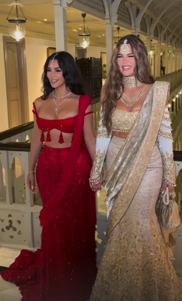 Kim Kardashian wearing a red skirt and crop top and Khloe Kardashian wearing a long white and gold gown