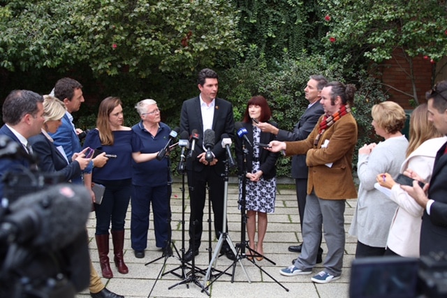 A wide shot of Scott Ludlam flanked by colleagues and reporters in the Fern Garden at WA's Parliament House.