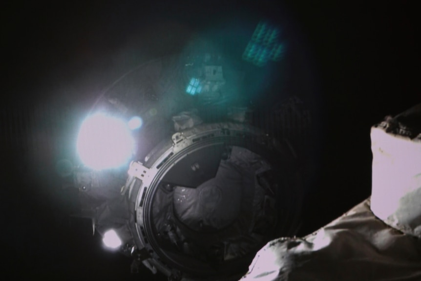 The docking station of a round spacecraft is illuminated by a bright light against the black background of space.