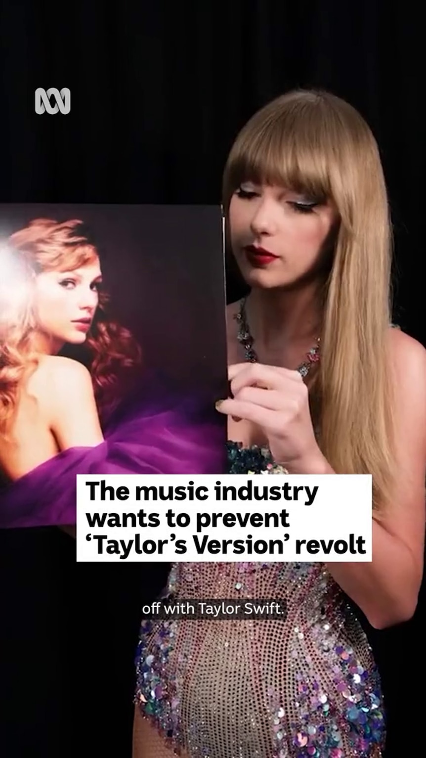 Taylor Swift stands in front of a black background holding a record featuring a photograph of her on the cover 