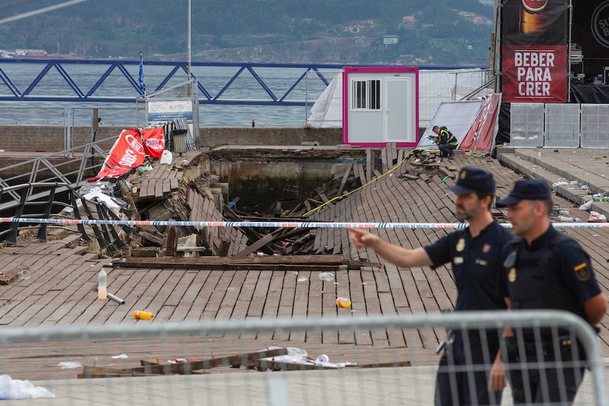 Two police officers walk past a collapsed oceanside baordwalk