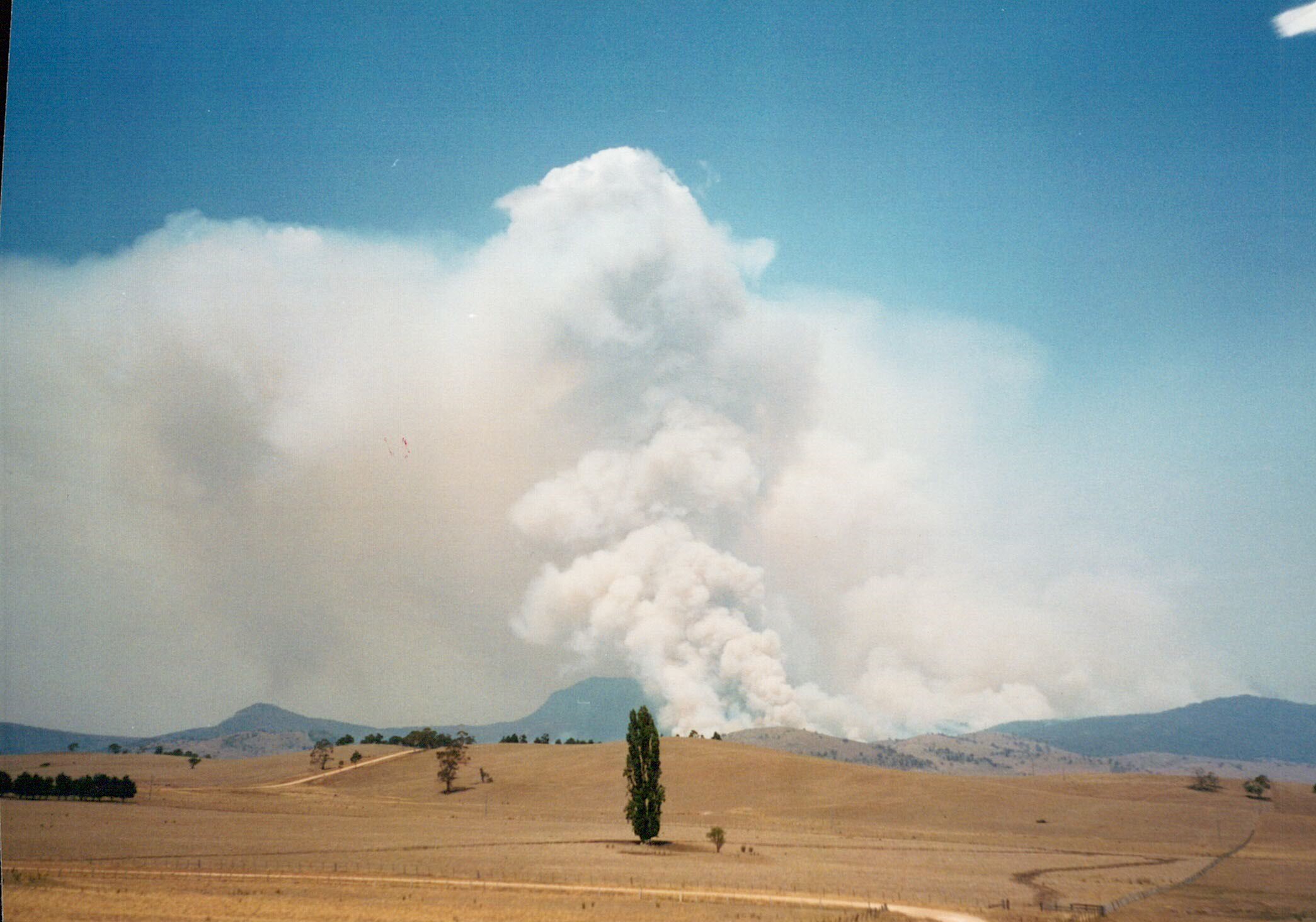 Dry ground with a large plume of smoke in the background from fire.