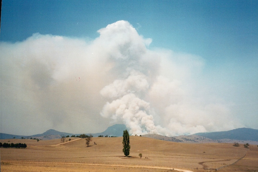 Dry ground with a large plume of smoke in the background from fire.