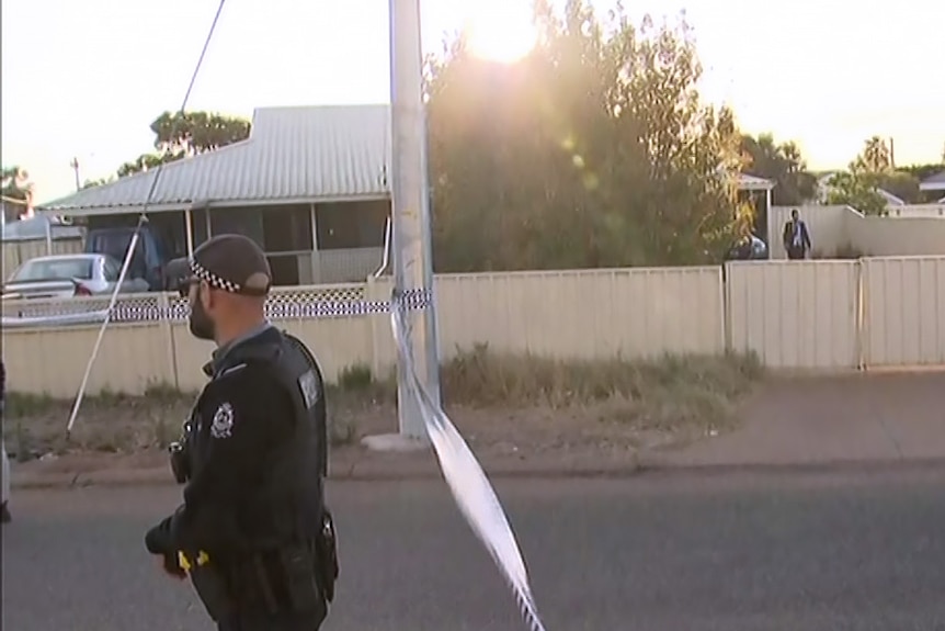 A police officer stands guard near police tape outside a house on a street in Carnarvon.