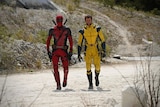 Comic book characters Deadpool and Wolverine walk towards the camera in full costume.