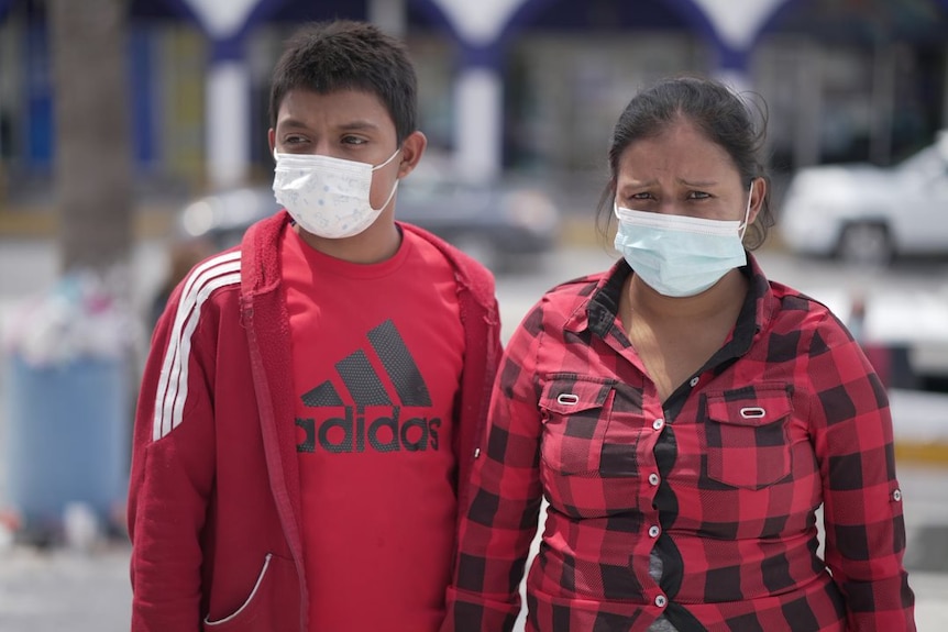 A woman wearing a red shirt and mask stands next to a boy wearing a red shirt and jumper and a mask.