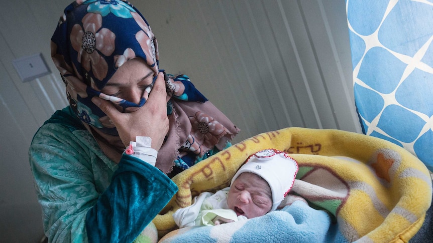 A woman looks down at a newborn baby swaddled in blankets.