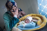 A woman looks down at a newborn baby swaddled in blankets.