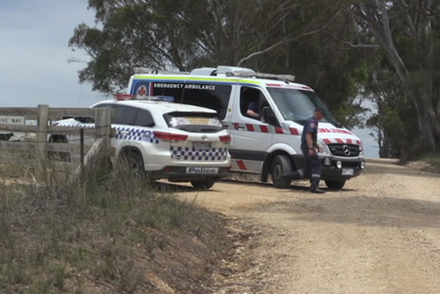 A police vehicle and an ambulance stationed at a gate on a dirt road.