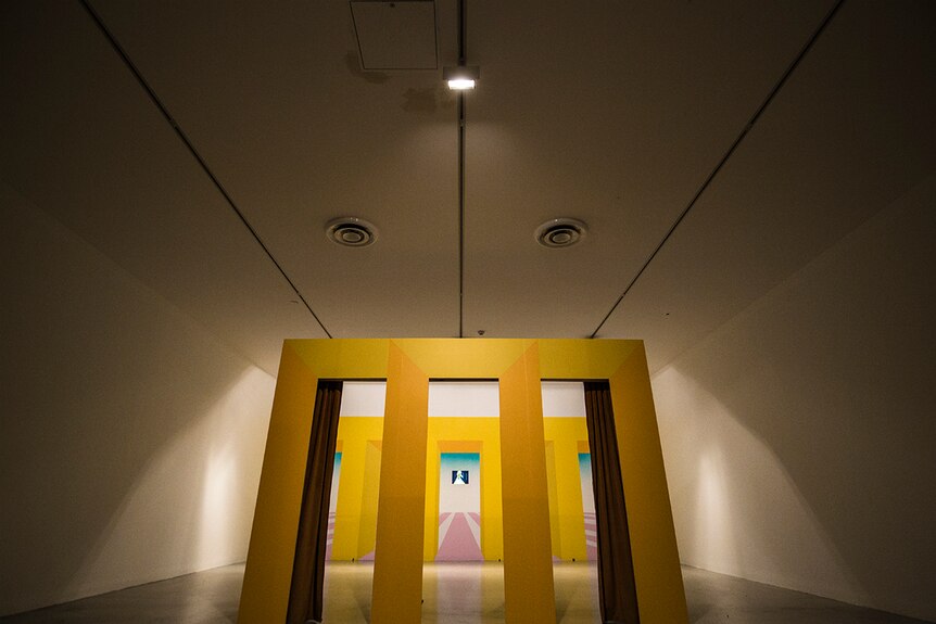 Colour photograph of yellow panelled fascade in front of yellow, pink and aqua painted walls in Campbelltown Art Gallery.