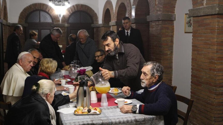 Men pour themselves a drink at a table with Pope Francis