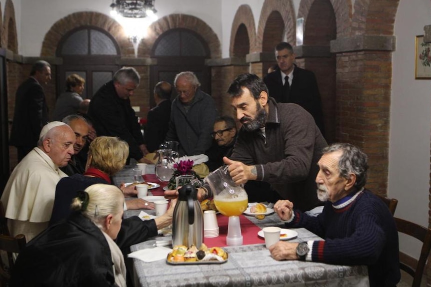 Men pour themselves a drink at a table with Pope Francis