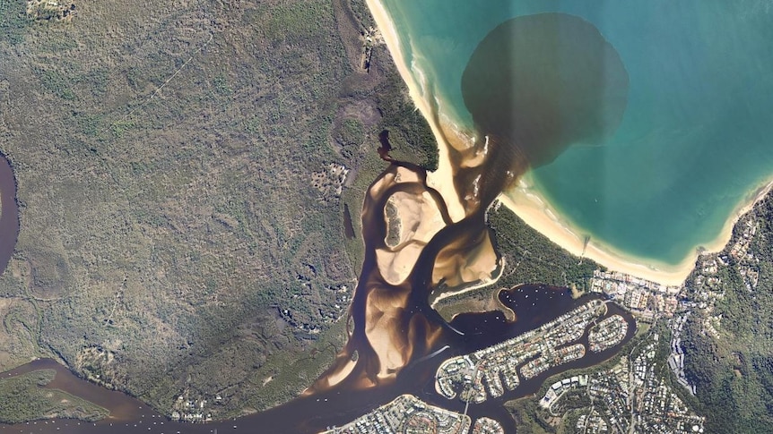 An aerial showing a brown river and plume of silt in the ocean.